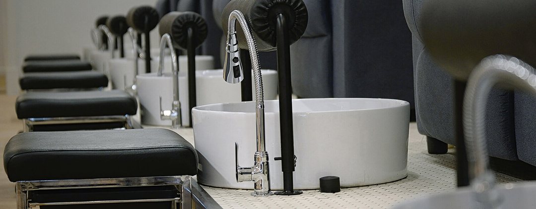 A real POSH photo: a row of clean white pedicure basins with chrome taps and black footrests. No words on it.
